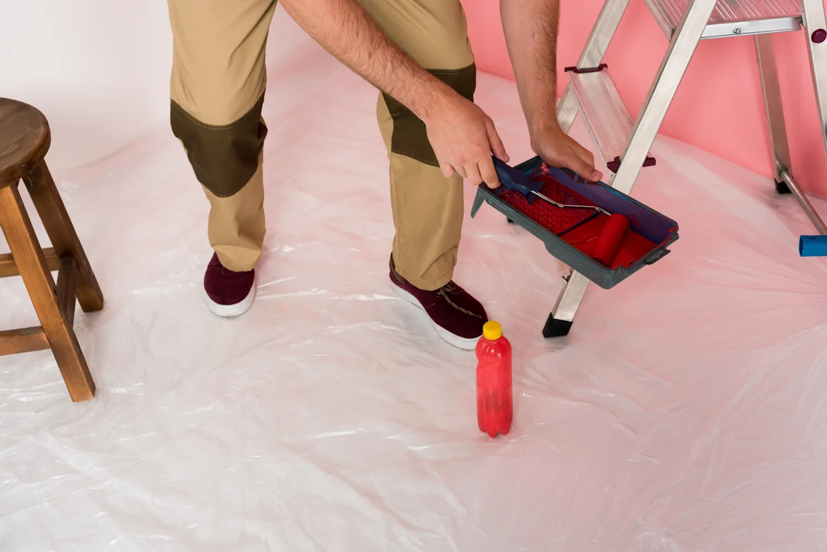 Un homme avec une boîte de peinture sur un sol protégé par une bâche